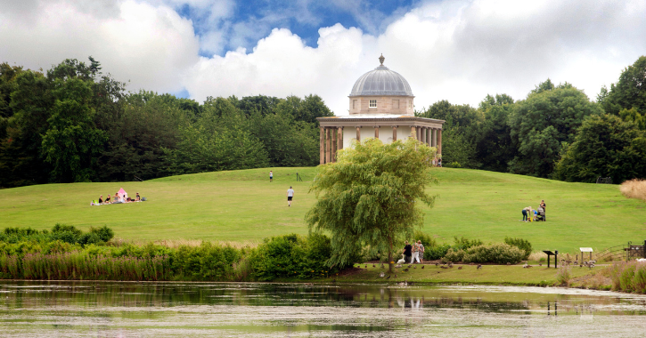 View of people walking past the lake and Temple of Minerva at Hardwick Countryside Park, Durham